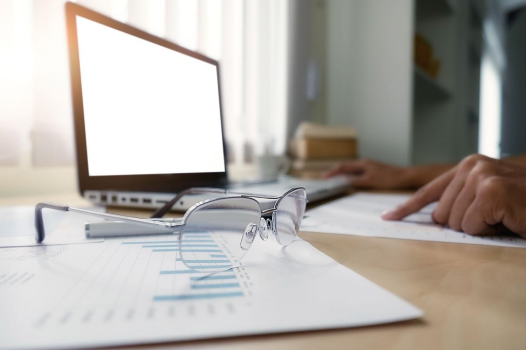 person looking at charts, a laptop and glasses